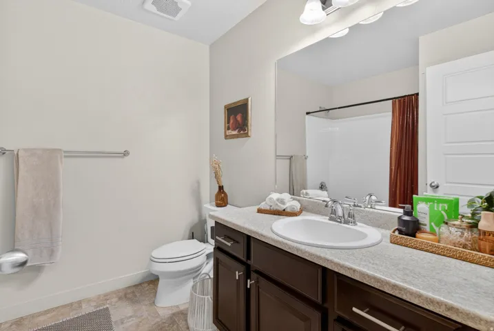 Bathroom featuring a single vanity with a solid surface countertop, an undermount sink, and dark wood cabinetry