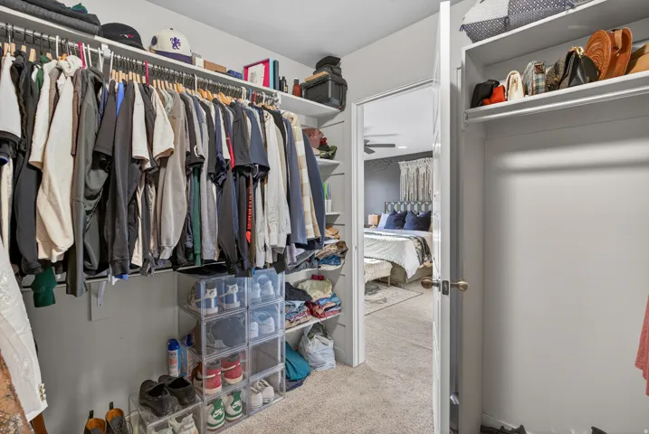 Walk-in closet featuring white built-in shelving, multiple hanging rods, and carpet flooring