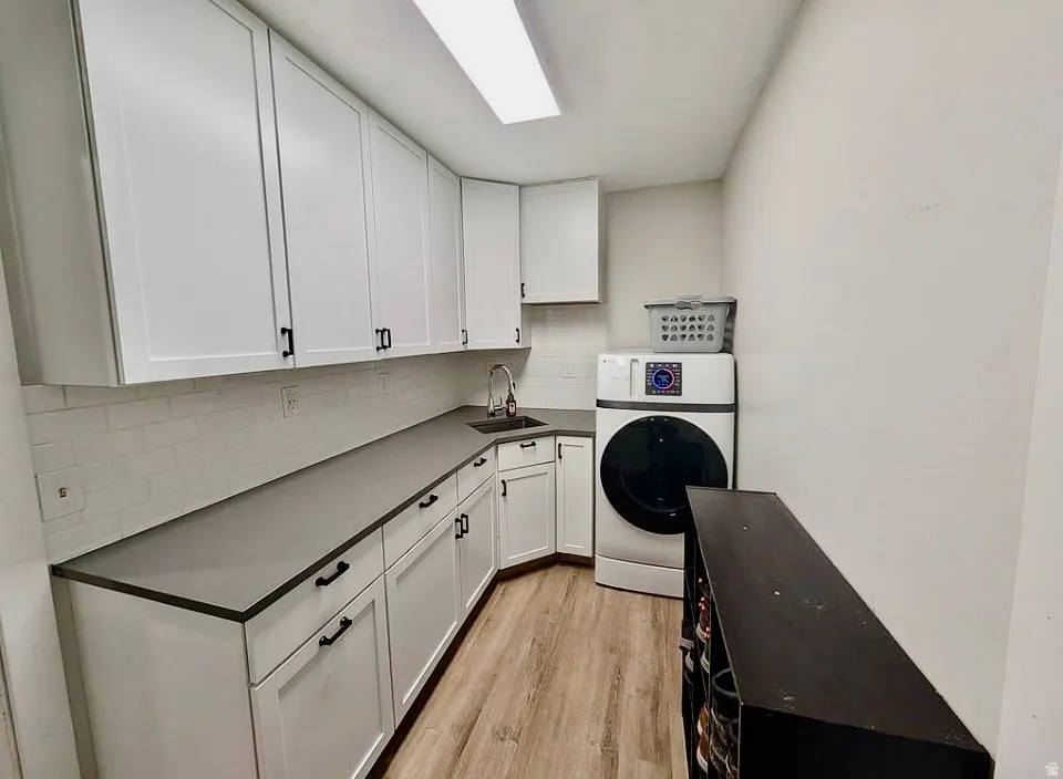 Utility room featuring extensive white cabinetry, dark countertops, a subway tile backsplash, and wood-finish flooring