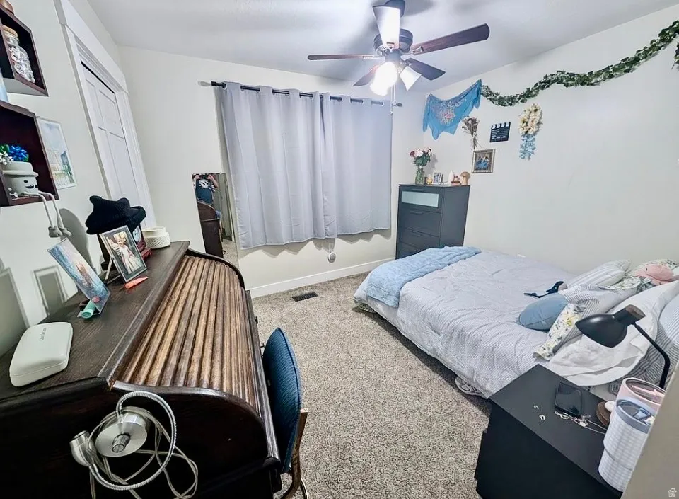Interior room featuring light neutral wall paint, carpet flooring, a ceiling fan with integrated lighting, and window with privacy coverings