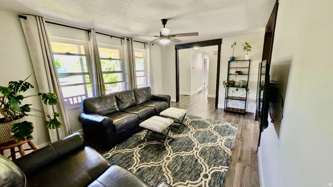 Living area featuring wood-finish flooring, a ceiling fan with integrated lighting, and white walls