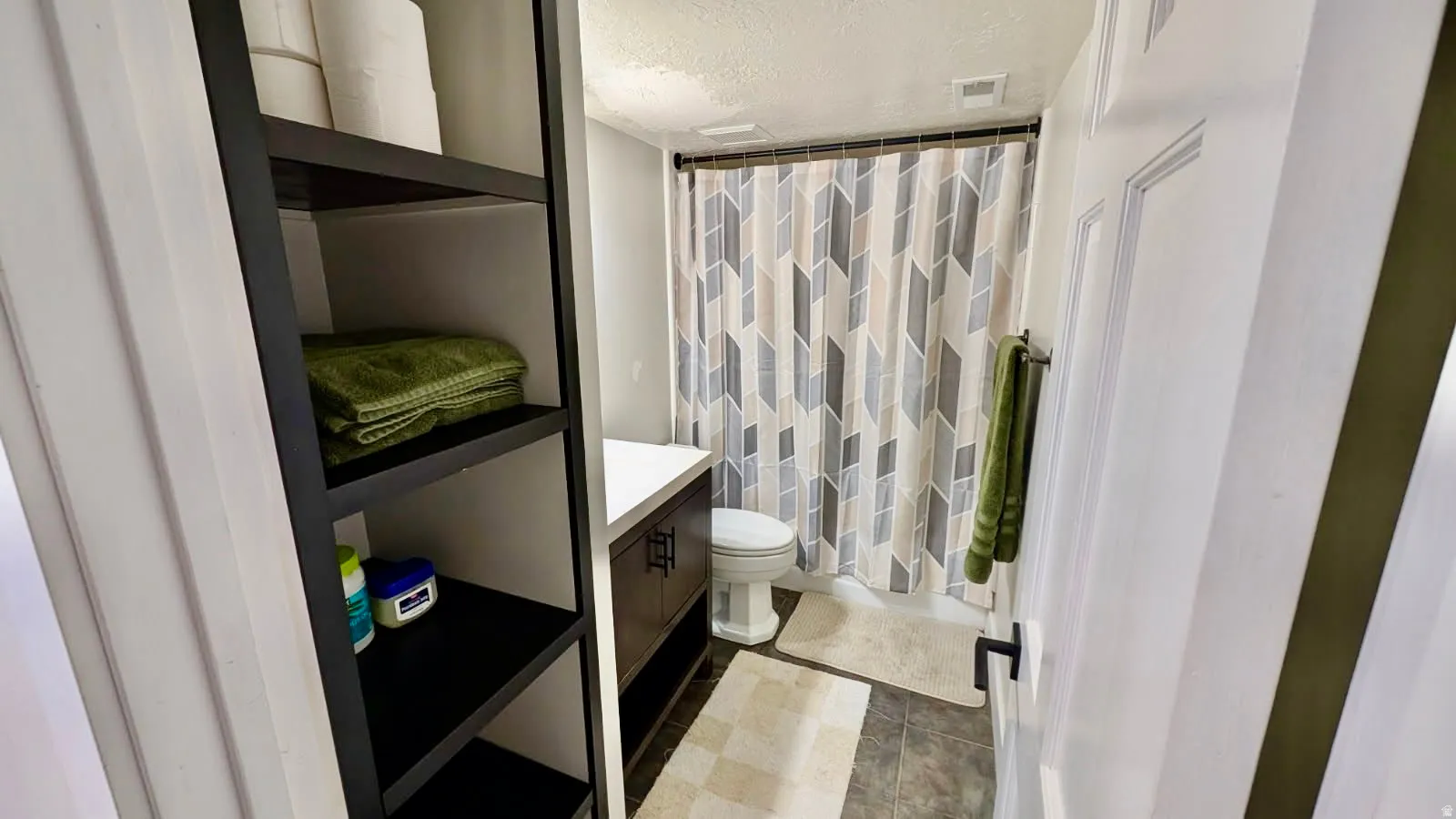 Compact bathroom featuring a dark wood-finish vanity with a white countertop and a geometric pattern shower curtain