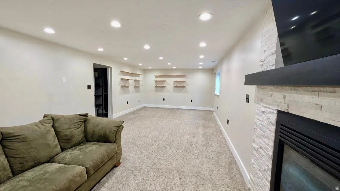 Expansive room featuring recessed lighting, carpet flooring, a built-in fireplace with a stone surround, a black mantle, and floating wood shelves