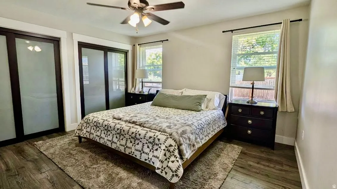 Recessed bedroom featuring wood-finish flooring, a ceiling fan, and two windows with blinds