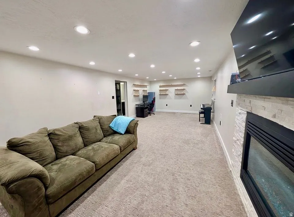 Spacious living area featuring recessed lighting, carpet flooring, a built-in fireplace with a stone surround, and floating wall shelves