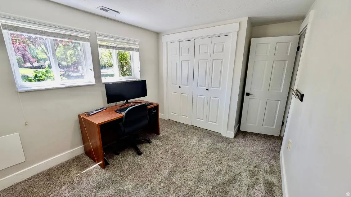 Carpeted room featuring two white-framed windows, white baseboards, and a built-in closet with bi-fold doors