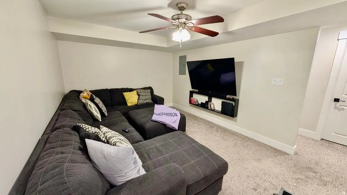 Carpeted recreation room featuring a recessed ceiling, ceiling fan with light fixture, and a wall-mounted entertainment shelf