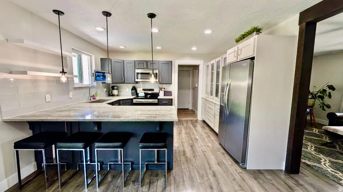 Modern kitchen featuring a breakfast bar with seating, gray cabinetry, light-toned countertops, and stainless steel appliances