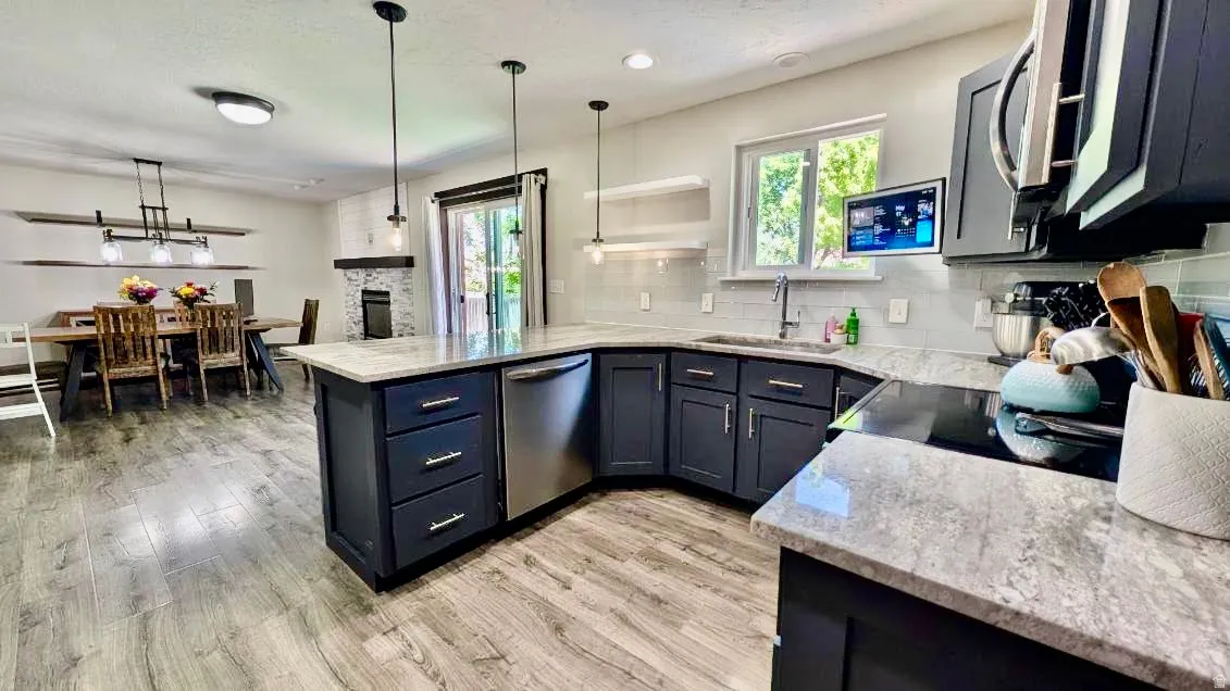 Modern kitchen featuring dark cabinetry, stone-finish countertops, stainless steel appliances, wood-finish flooring, and pendant lighting