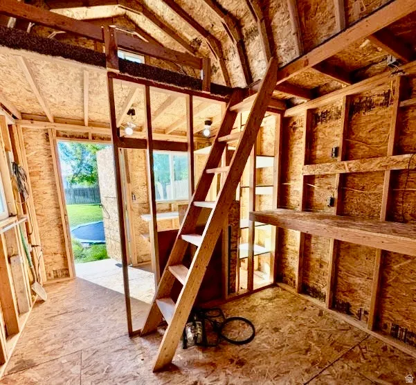 Unfinished interior space featuring exposed wood framing, oriented strand board walls and flooring, and a built-in wooden ladder providing access to an upper loft