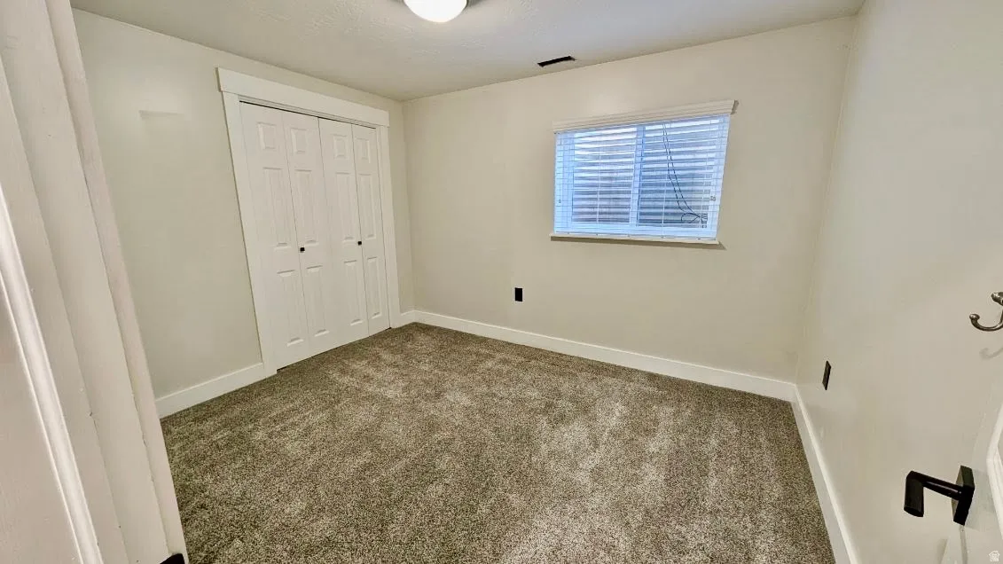 Neutral-toned room featuring a large bi-fold closet, textured carpeting, and a window with blinds