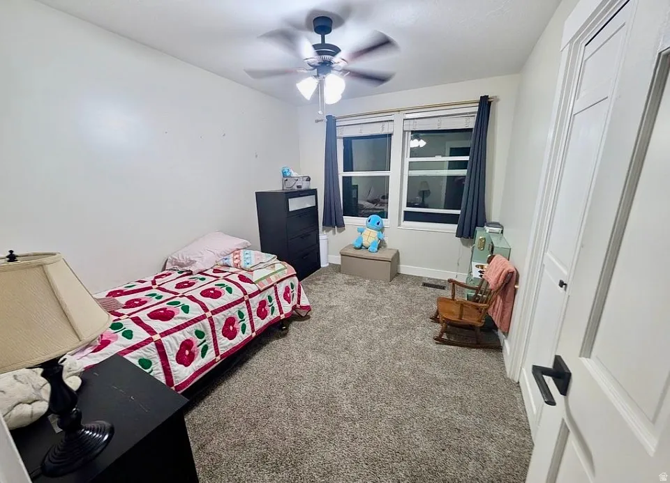 Carpeted interior space featuring a ceiling fan with integrated lighting, a window with dark drapes, and a white interior door with matte black hardware