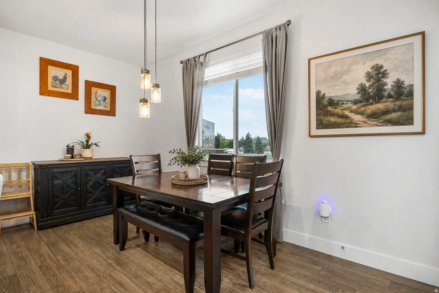 Dining area featuring wood-finish flooring, a contemporary pendant light fixture, and a large window with privacy blinds