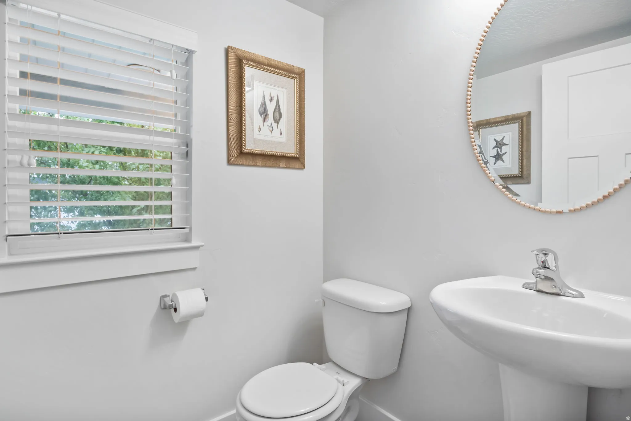 Pedestal sink with chrome faucet, toilet, and a window with white blinds