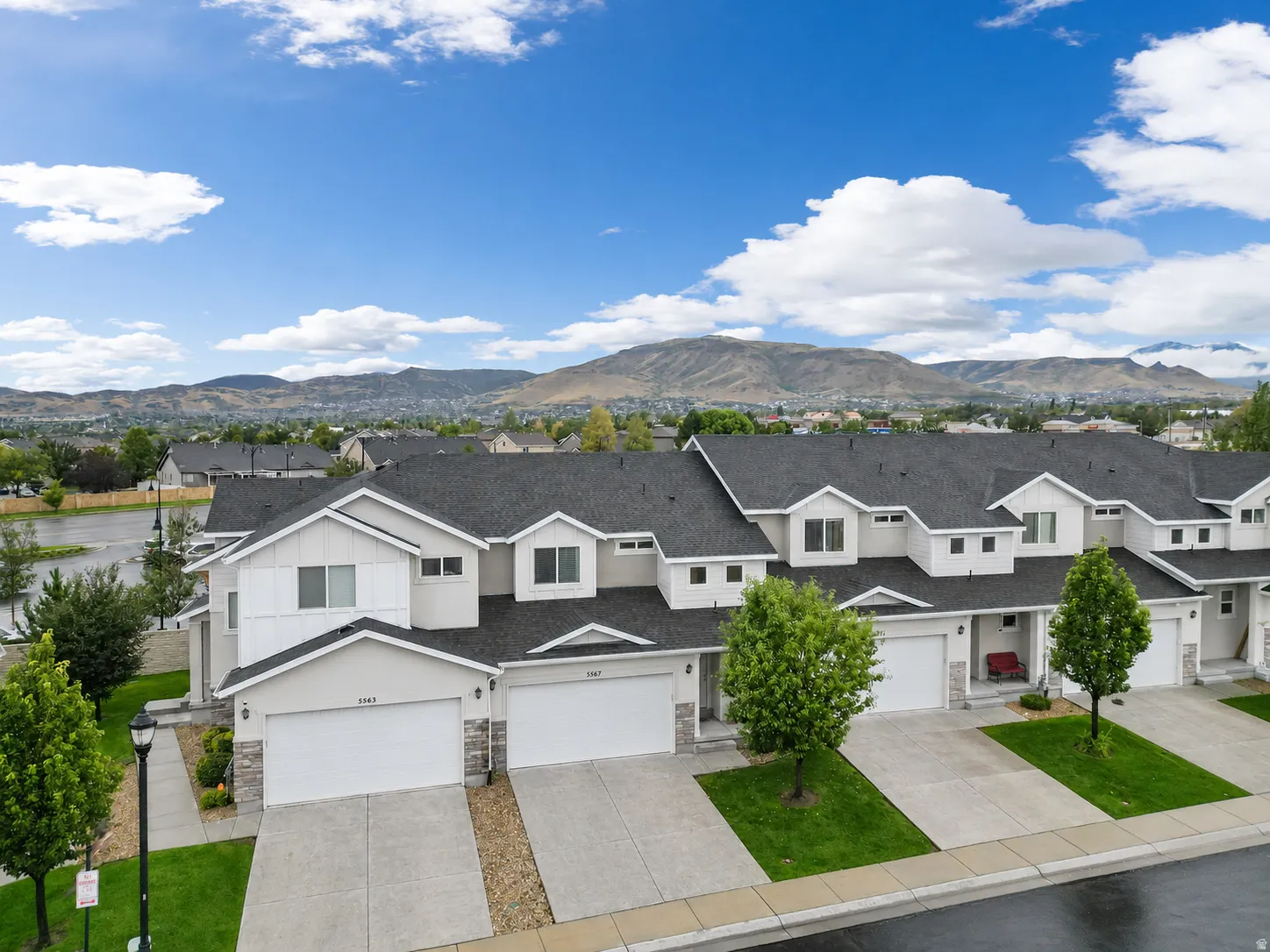 Exterior features include a multi-unit residential building with a dark gray shingle roof, light-colored siding, and white garage doors