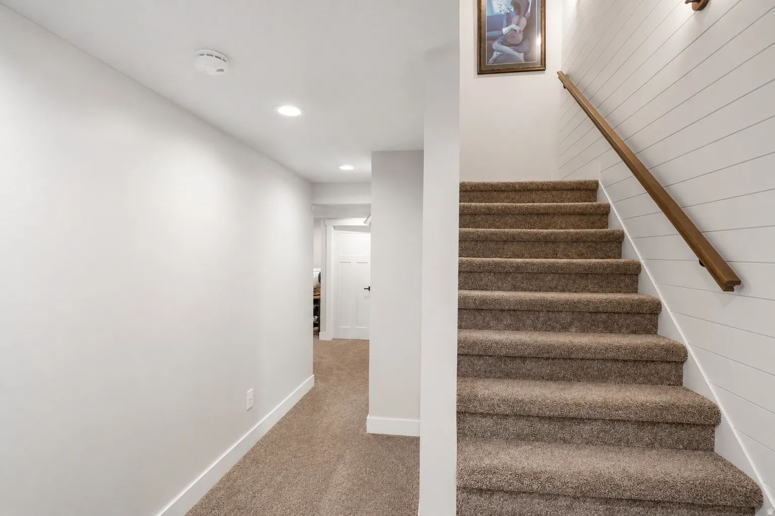 Carpeted staircase with a wood handrail and shiplap wall detail