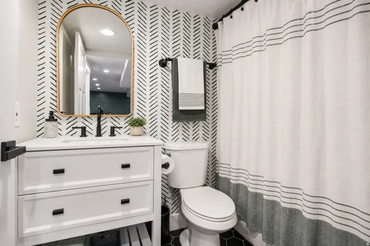 Bathroom featuring a white vanity with a rectangular basin and black hardware, set against patterned wallpaper
