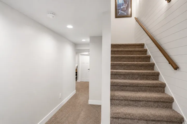 Carpeted staircase with a wood handrail and shiplap wall detail