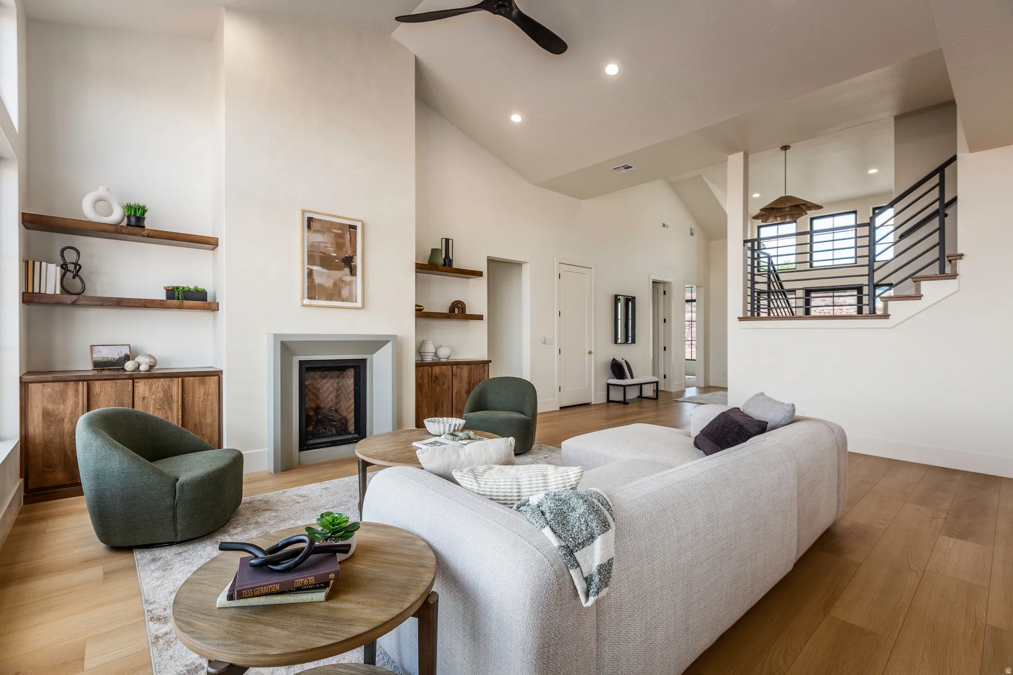 Spacious living area featuring high vaulted ceilings, light wood-finish flooring, a contemporary fireplace with a sleek surround, built-in cabinetry, and open shelving