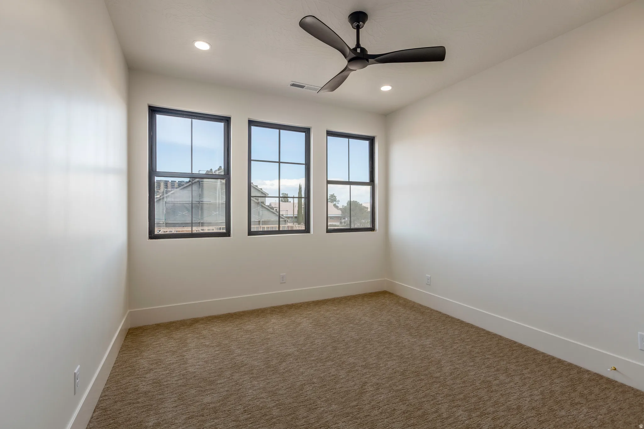 Carpeted room featuring three dark-framed windows, a matte black ceiling fan, and recessed lighting