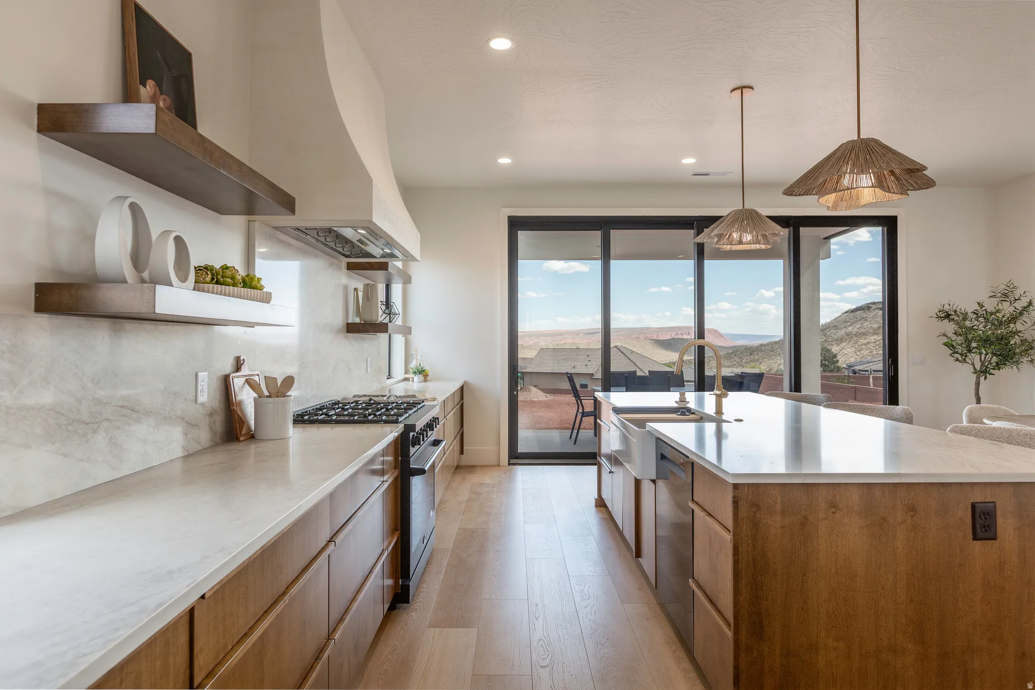 Modern kitchen featuring a large island with an undermount sink and golden faucet, light wood-finish flooring, and light-toned cabinetry