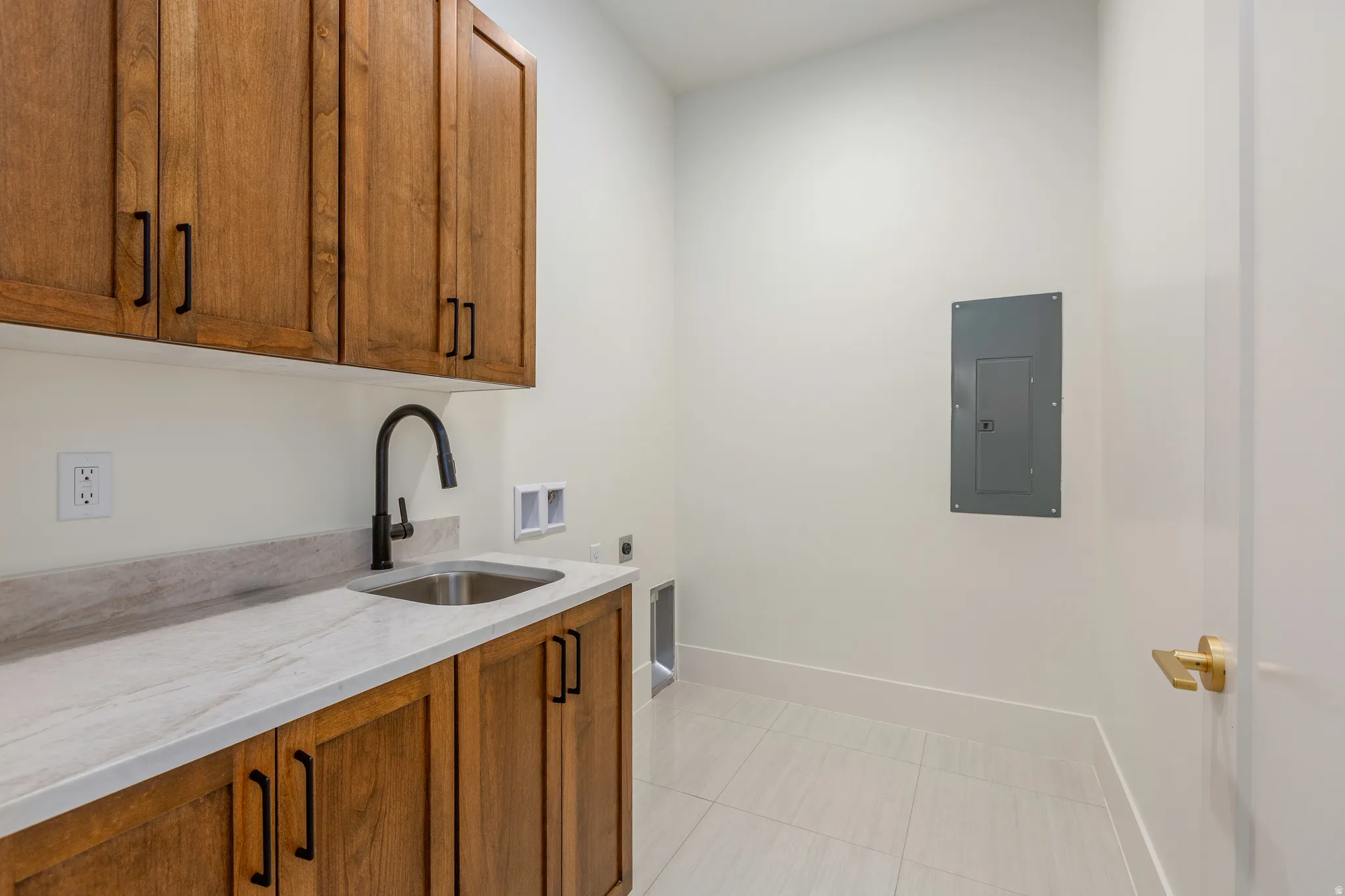 Utility space featuring wood-finish cabinetry, a stainless steel sink with a matte black faucet, and light-toned countertops