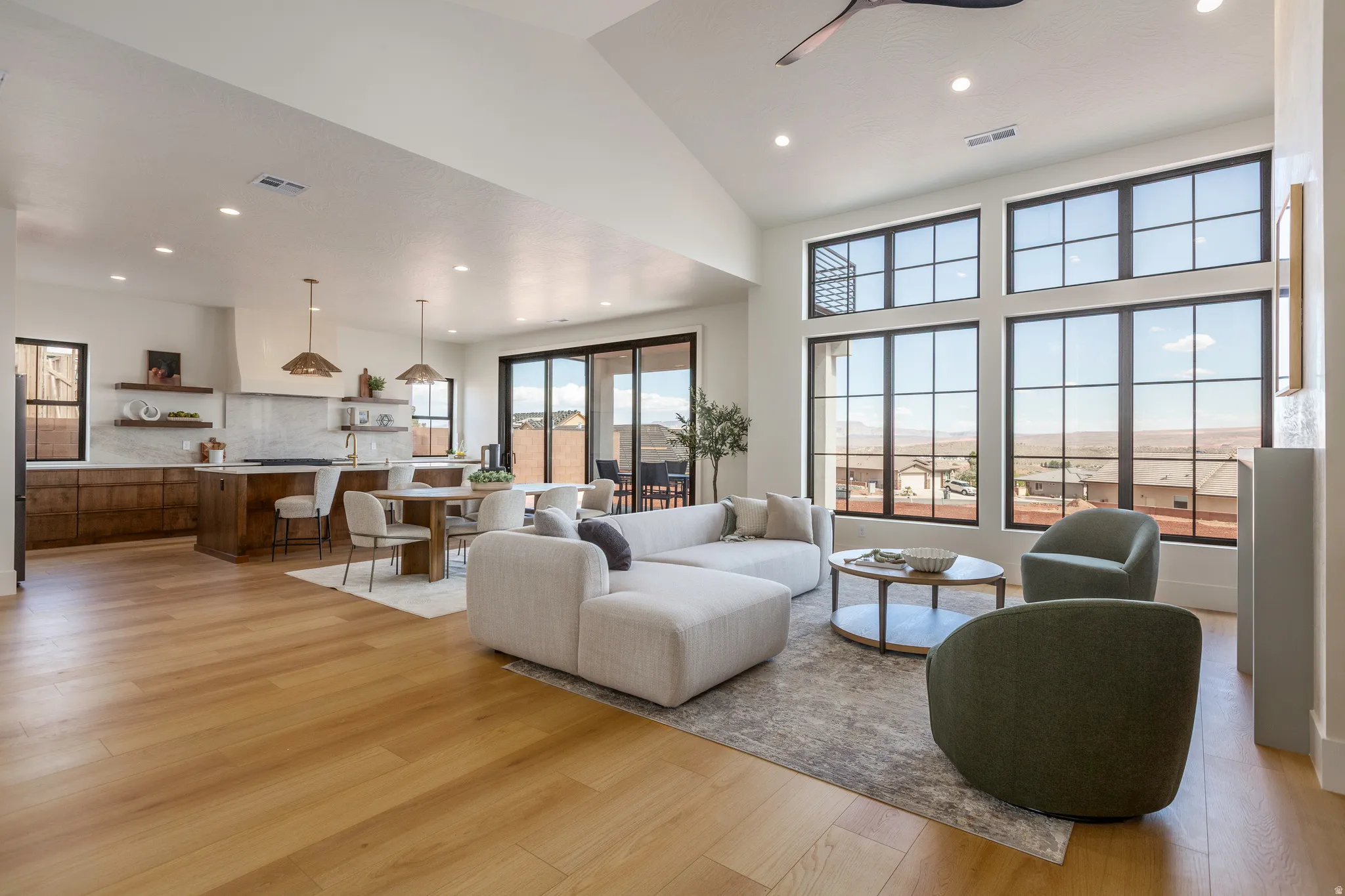 Spacious living area featuring expansive grid-pattern windows, a vaulted ceiling with recessed lighting, and light wood-finish flooring