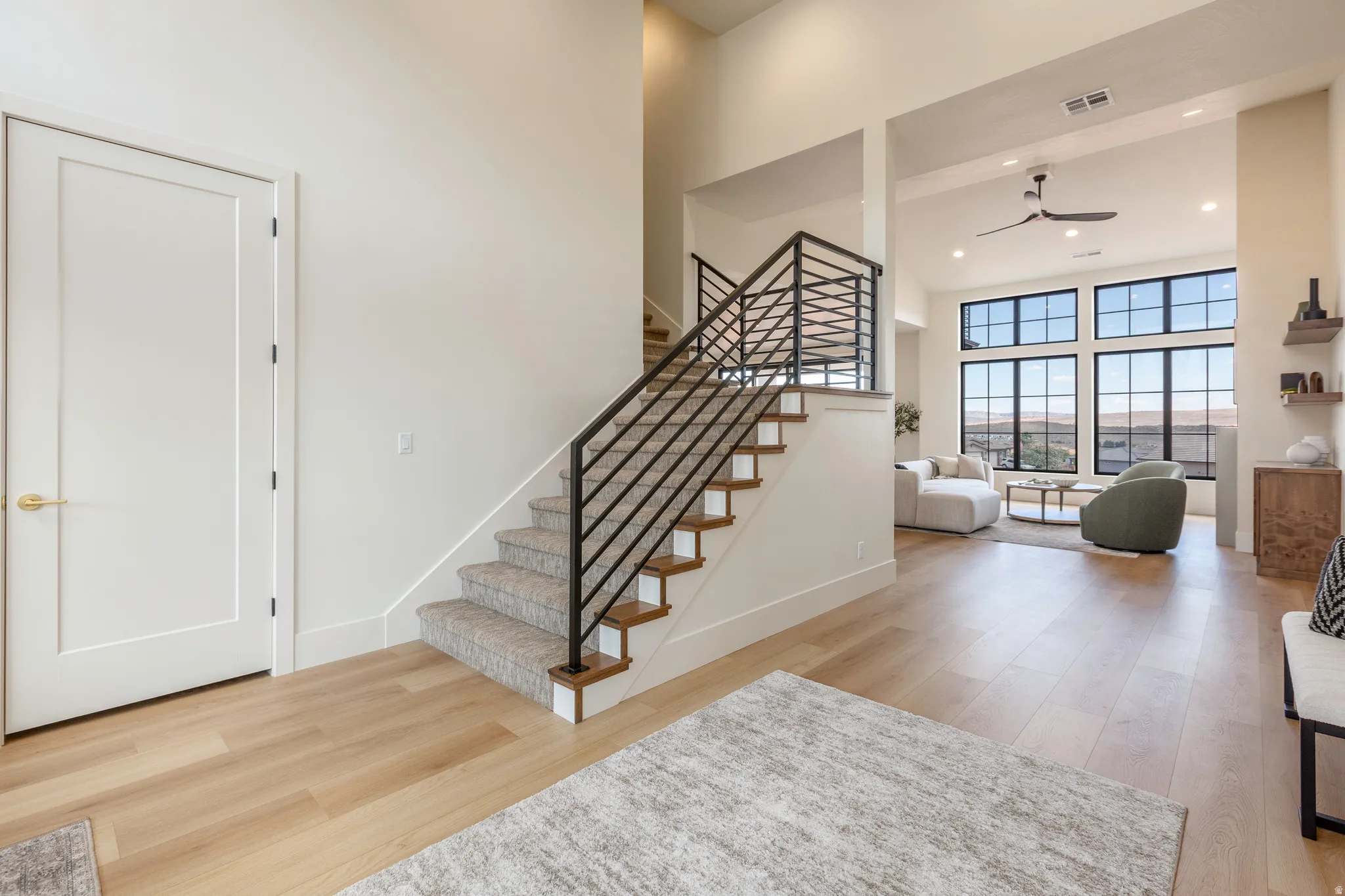 Modern staircase with black metal railings, light wood-finish flooring, high ceilings, large multi-pane windows, and recessed lighting