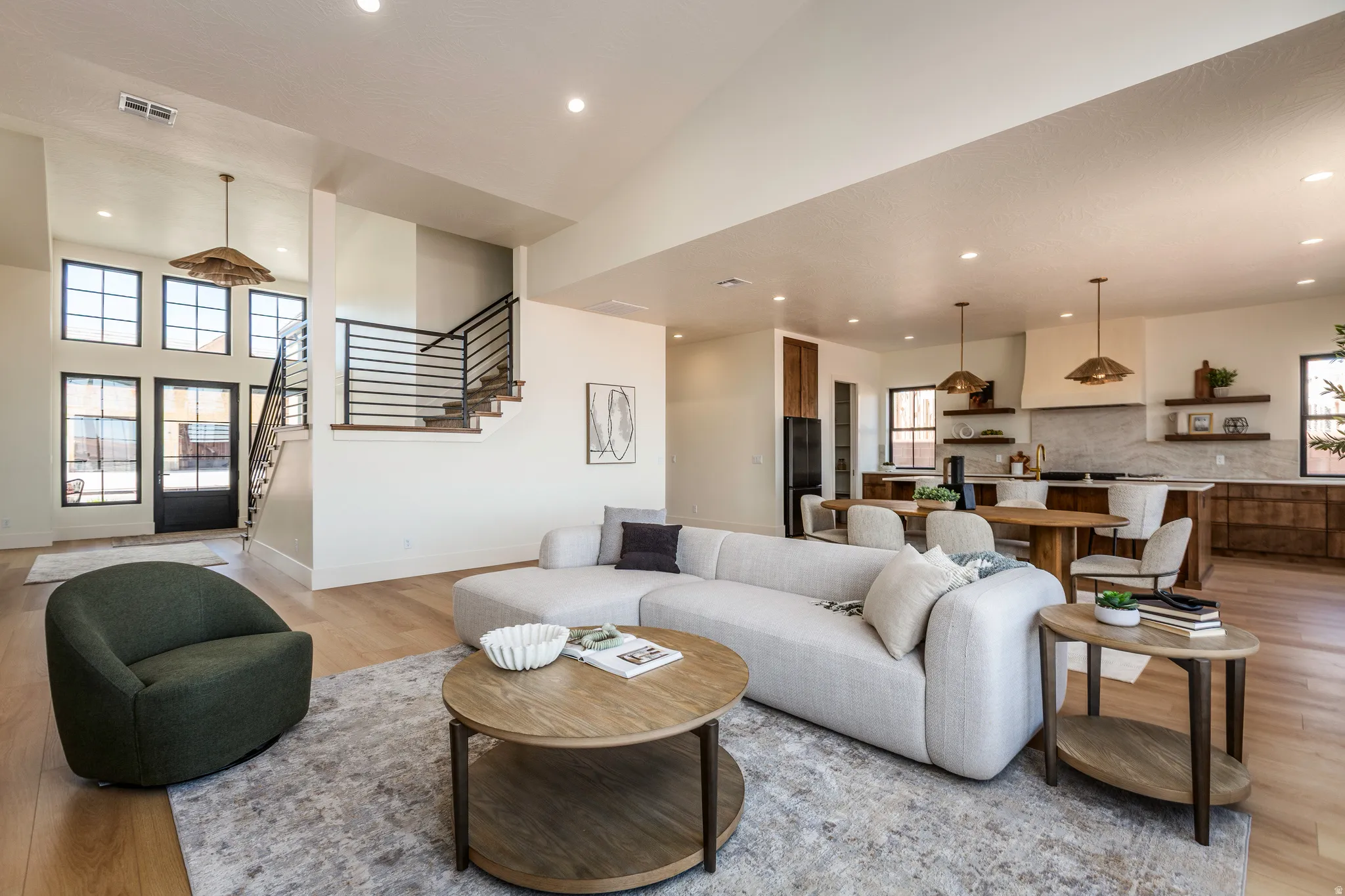 Open-concept living space featuring wood-finish flooring, recessed lighting, and a modern staircase with horizontal metal balusters