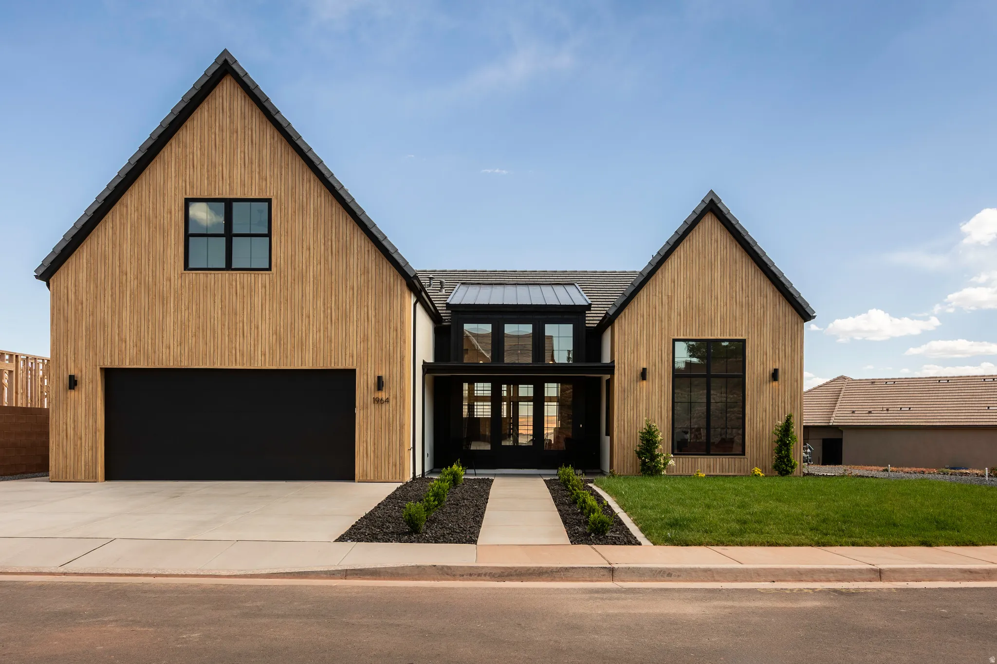 Modern farmhouse exterior featuring vertical wood-finish siding, black framed windows, a black garage door, a front lawn, and a concrete driveway