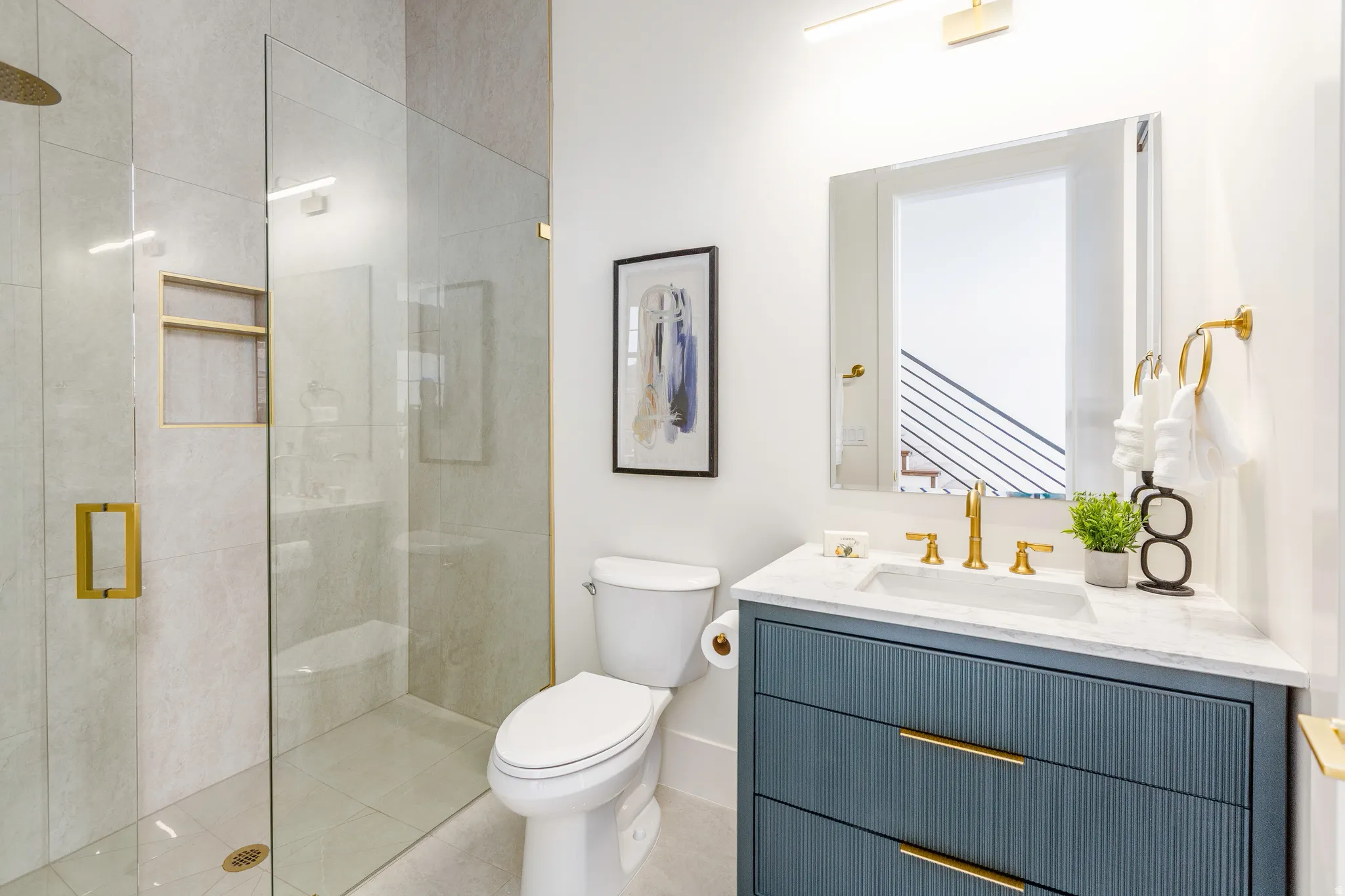 Modern bathroom featuring a glass-enclosed shower with gold-finish fixtures, a built-in shower niche, and light-toned wall tiling
