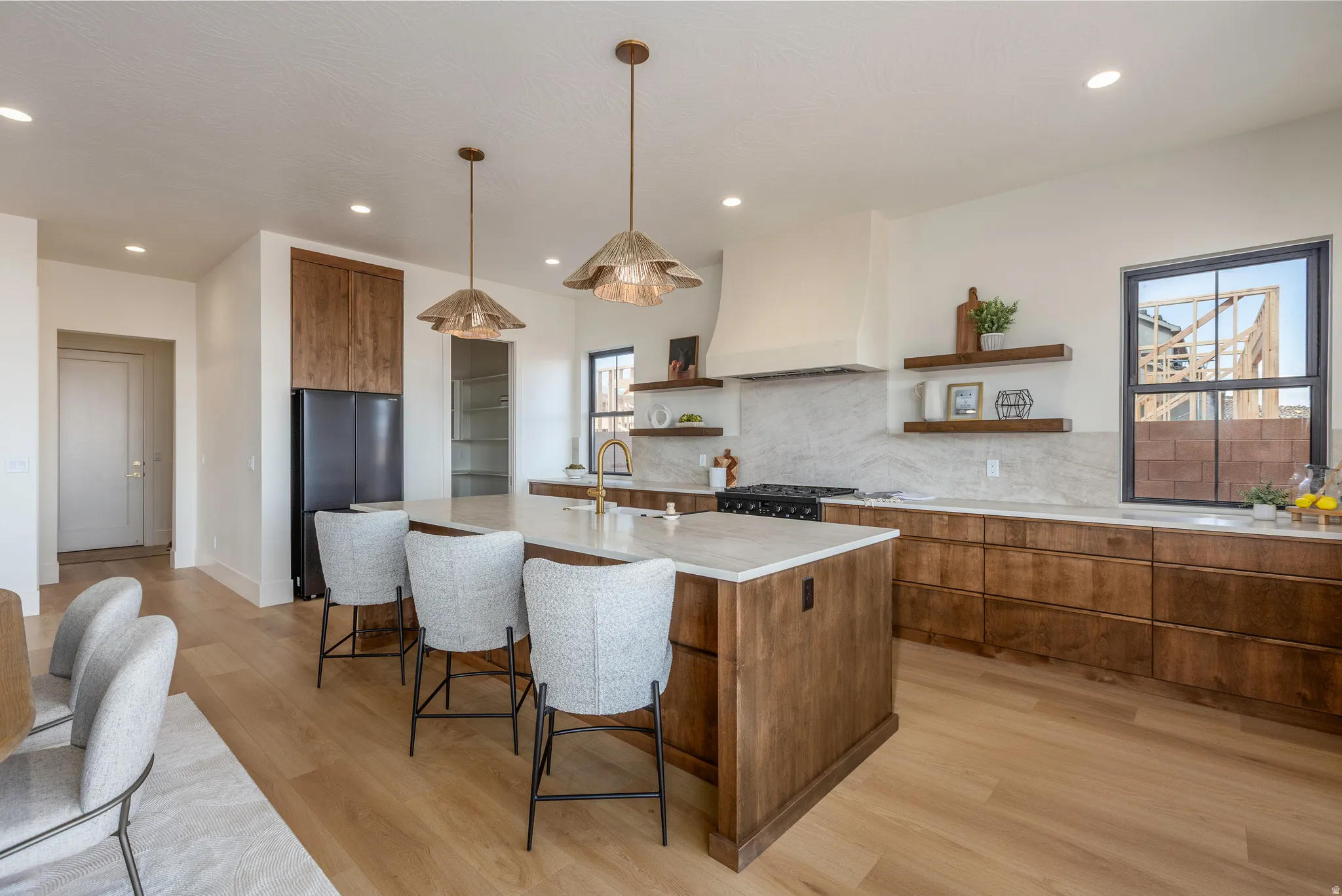 Spacious kitchen featuring a large central island, light wood-finish flooring, custom wood cabinetry, a built-in range hood, and a full-height tile backsplash