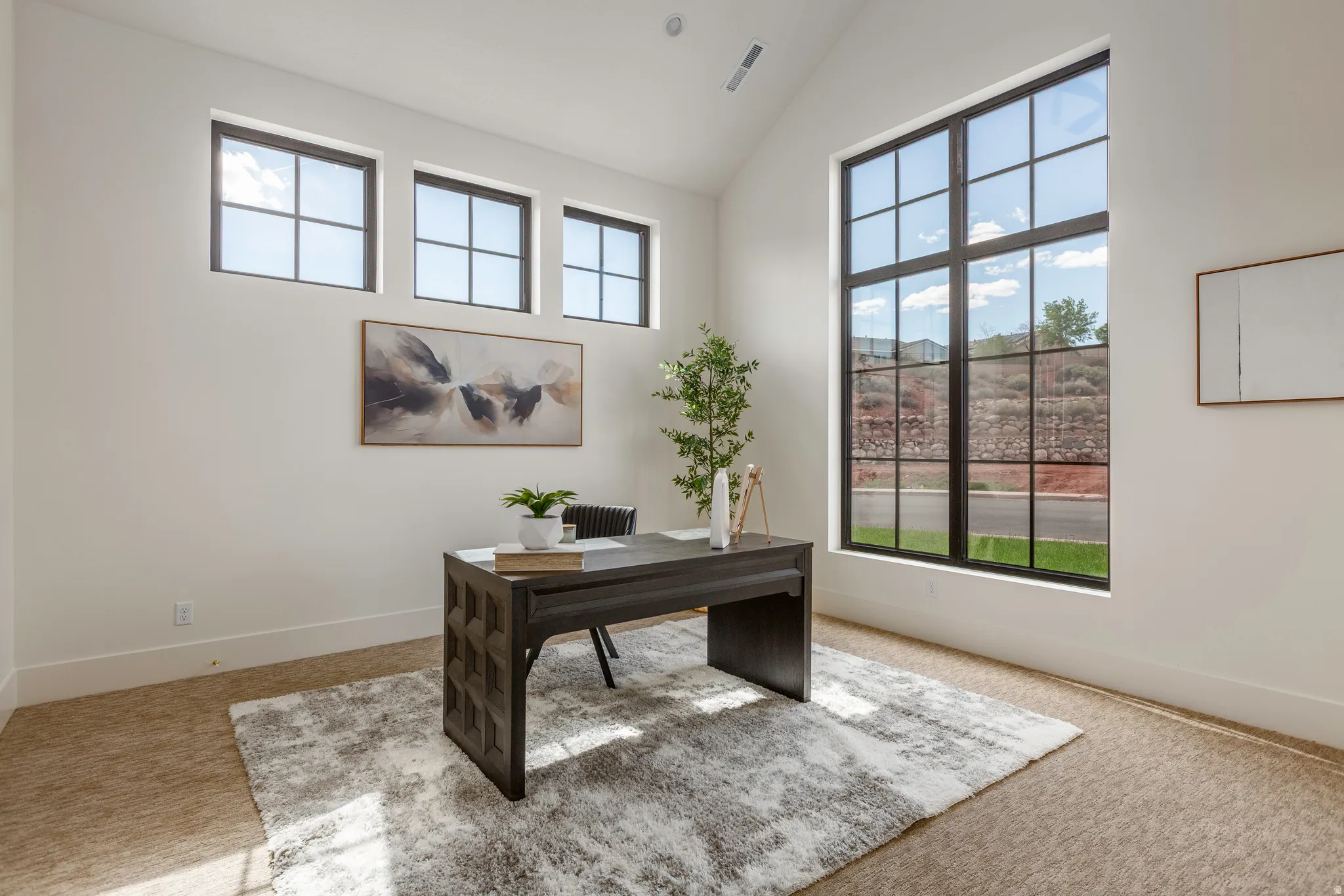 Vaulted ceiling room featuring a large grid window, three transom windows, light-toned walls, and carpet flooring