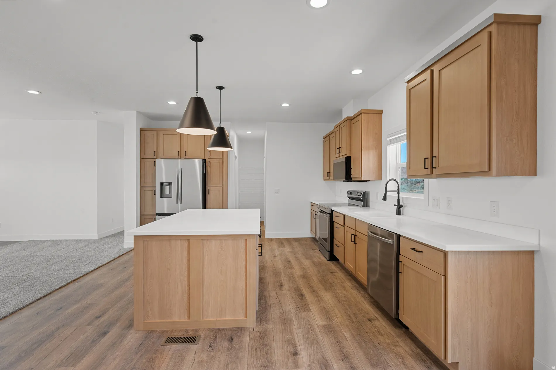 Open-concept kitchen featuring an expansive center island with a white countertop, wood-finish flooring, recessed lighting, and stainless steel appliances