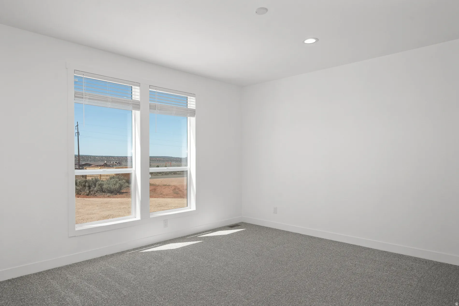 Bright interior space featuring dual windows with horizontal blinds, neutral wall paint, recessed ceiling lighting, and gray carpeting
