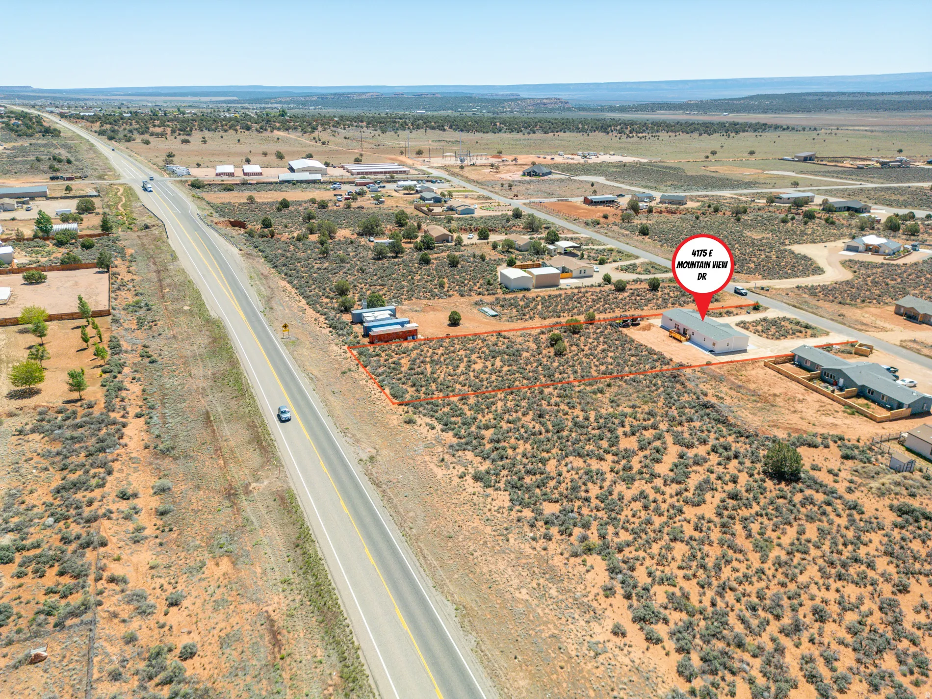 Spacious desert landscape featuring a marked lot boundary, a residential structure with a light-colored exterior, and proximity to a paved road