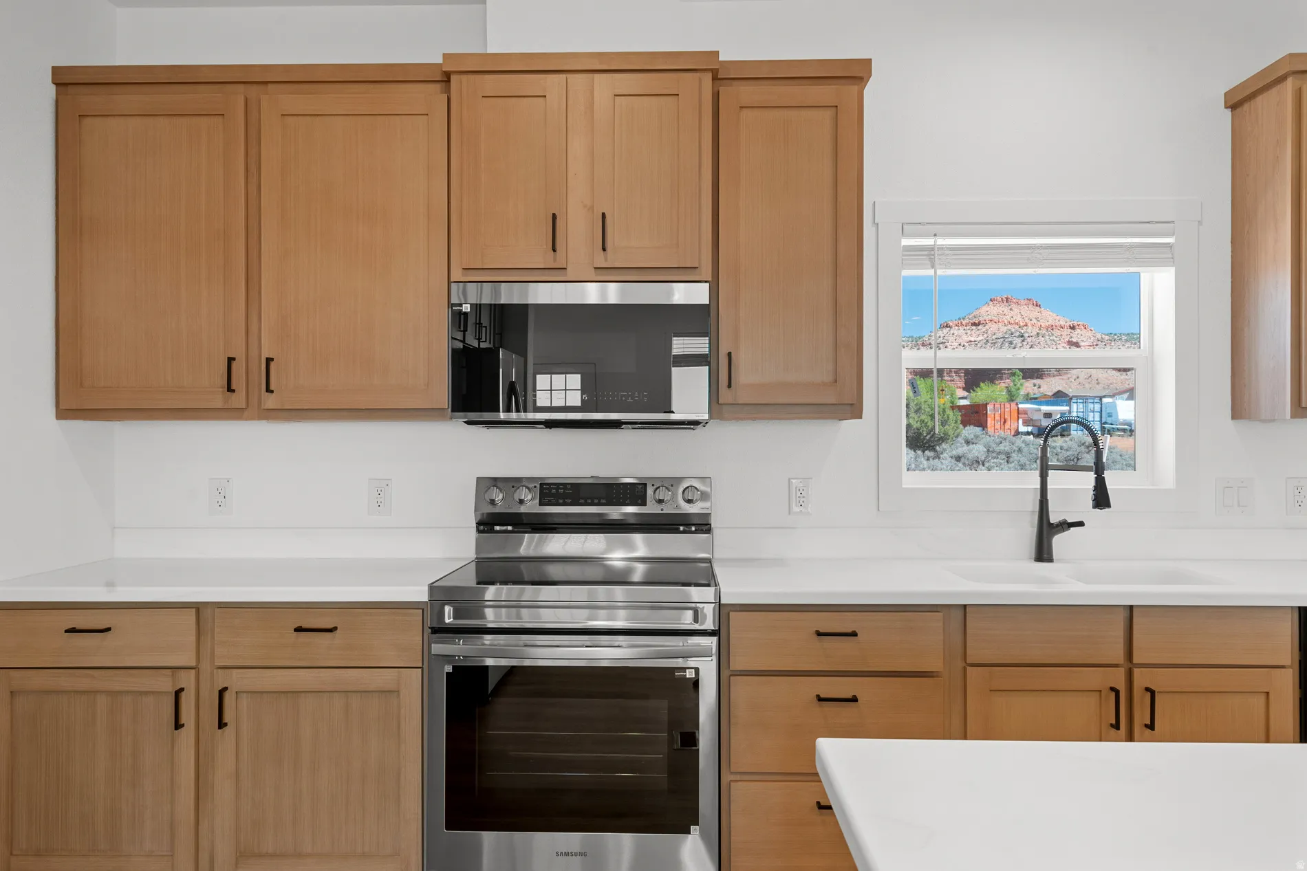 Modern kitchen featuring light wood cabinetry, a stainless steel range, a stainless steel built-in microwave, white countertops, and a window with mountain scenery
