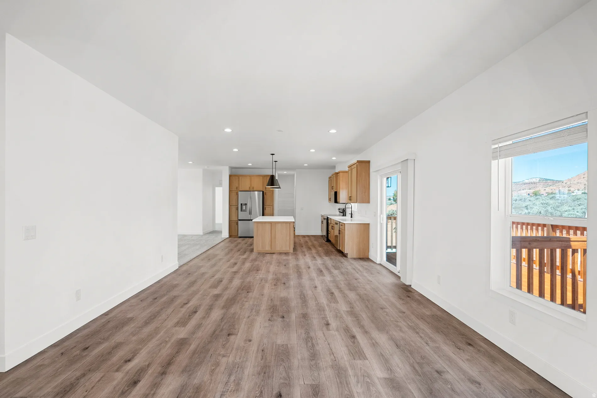 Spacious open-concept living area featuring wood-finish flooring, recessed lighting, and a kitchen with light wood cabinetry, white countertops, and a stainless steel refrigerator