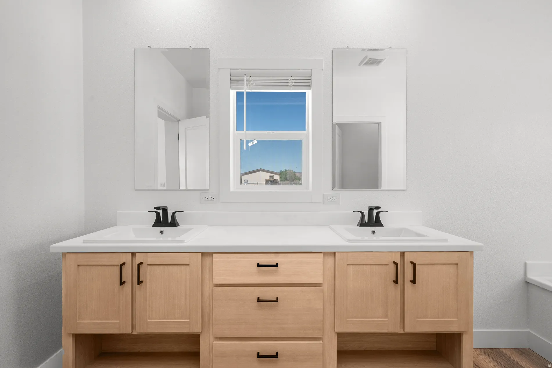 Double vanity with light wood-finish cabinetry, white countertops, and integrated rectangular sinks