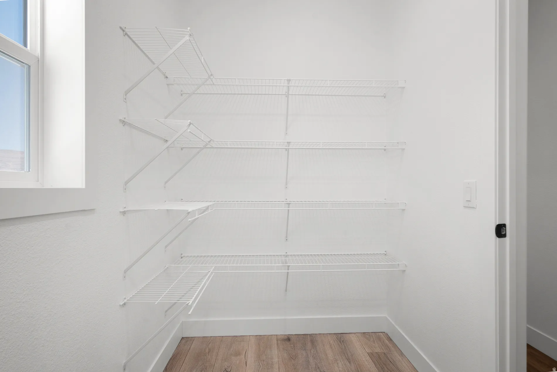 Walk-in closet with multi-level wire shelving, wood-finish flooring, and natural light from a window