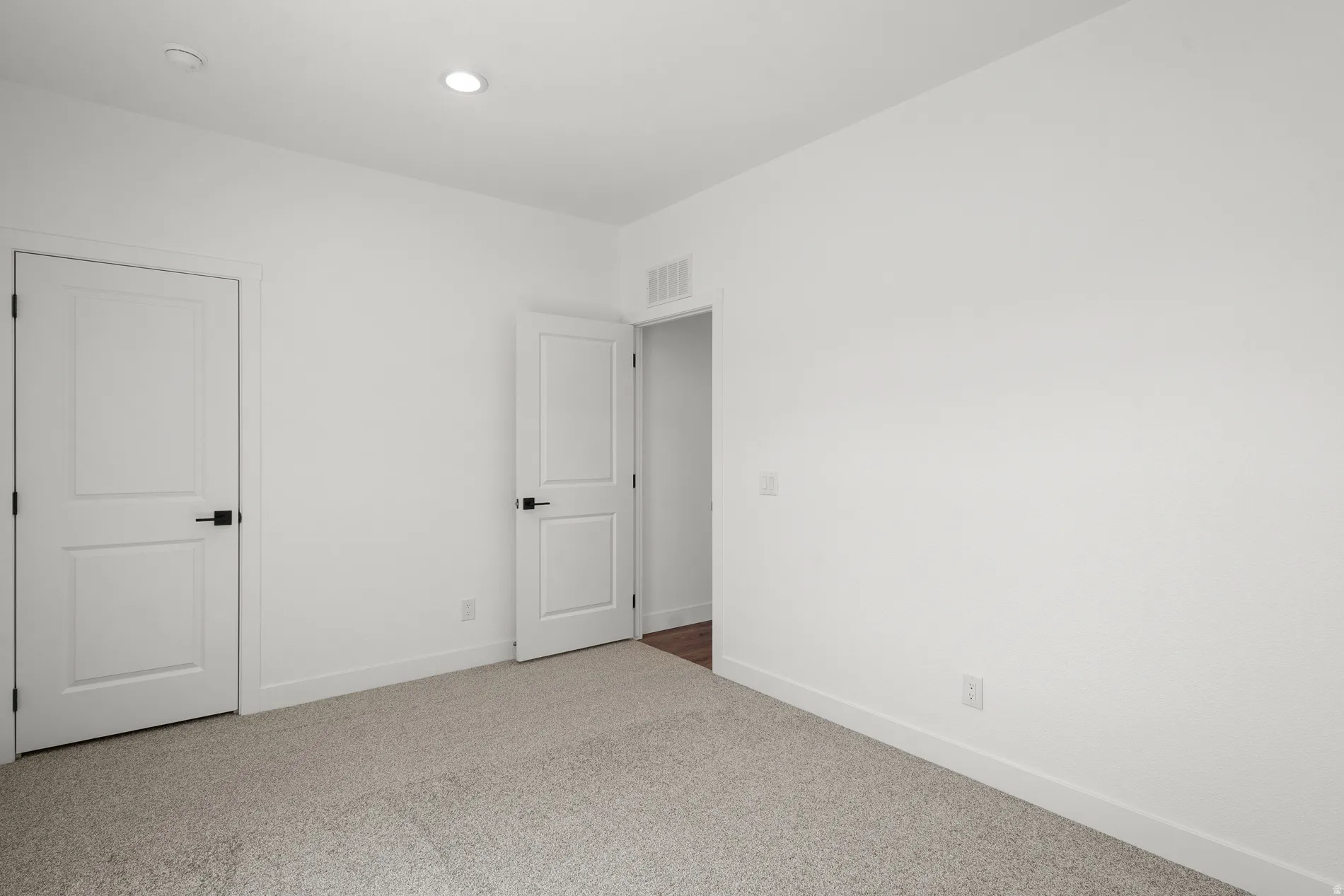 Carpeted room featuring white walls, white trim, and two paneled doors with matte black hardware