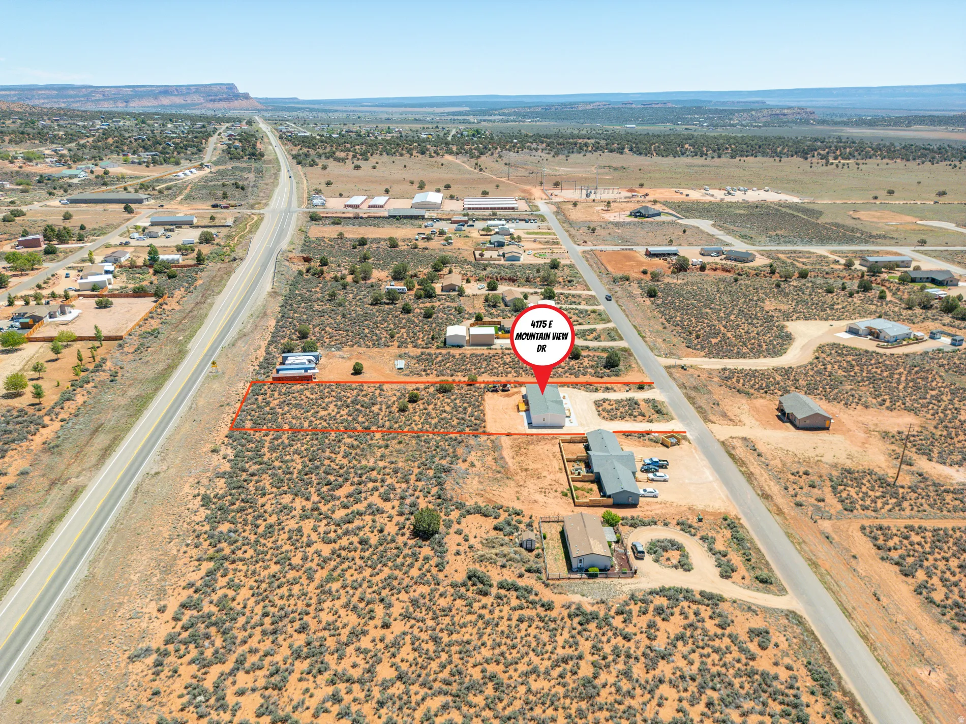 Expansive desert landscape with multiple residential structures and paved road access
