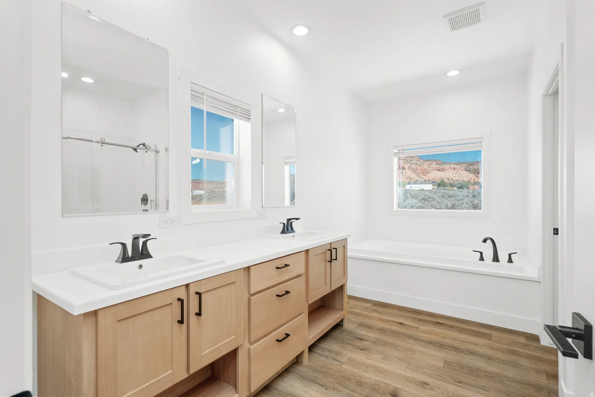 Dual vanity with light wood-finish cabinetry, white countertops, and matte black fixtures