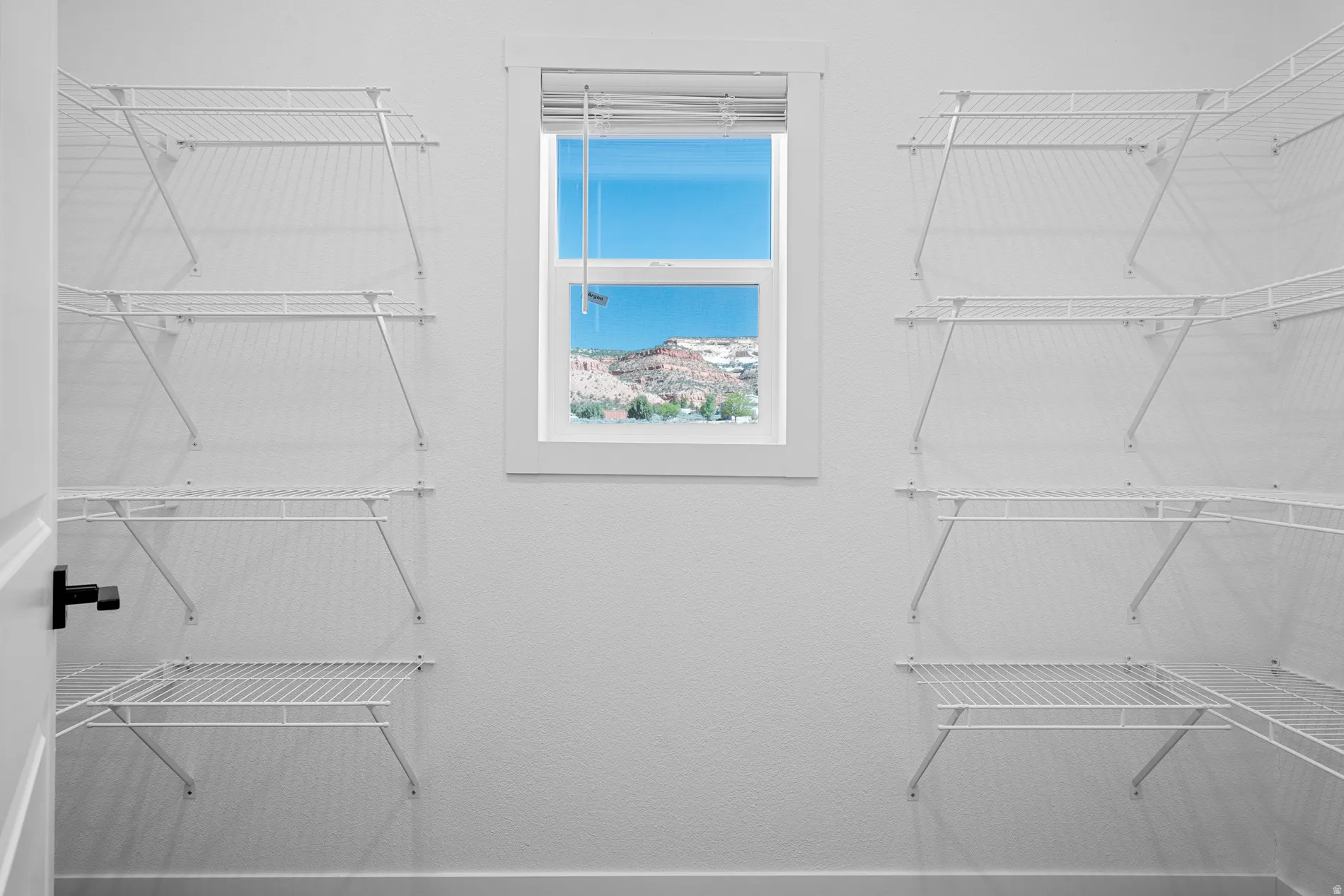 Walk-in closet with white wire shelving, central window, and white trim