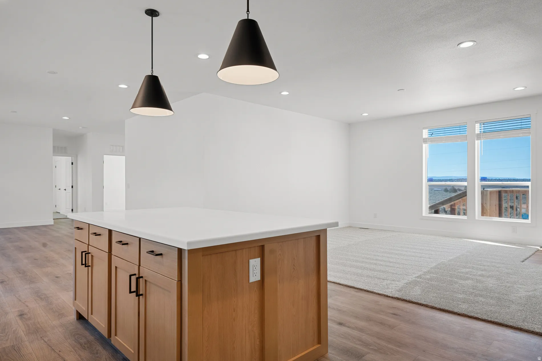 Kitchen island with light wood-finish cabinetry, white countertop, and matte black hardware