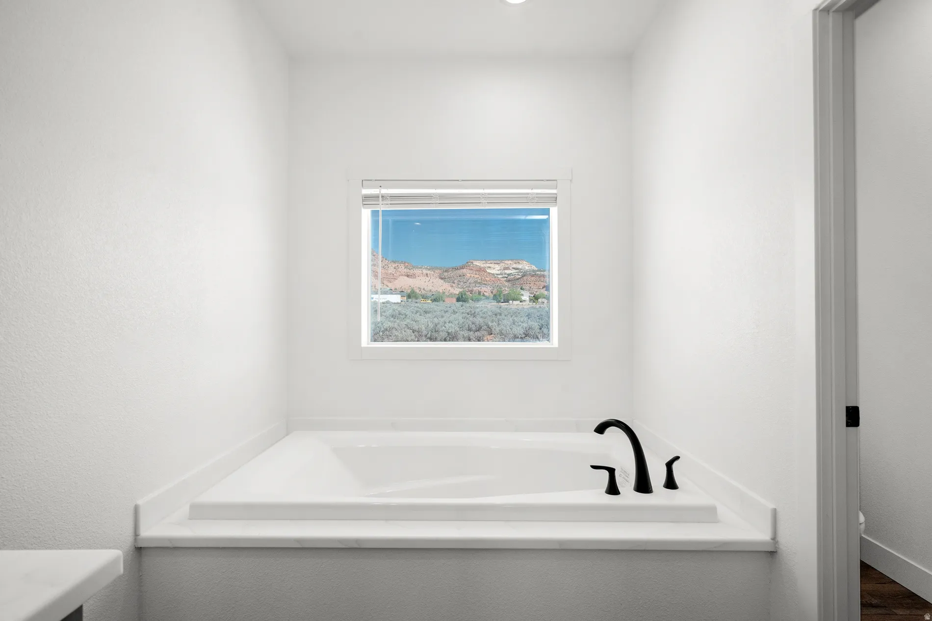 Soaking tub with white surround, black fixtures, and a window with horizontal blinds