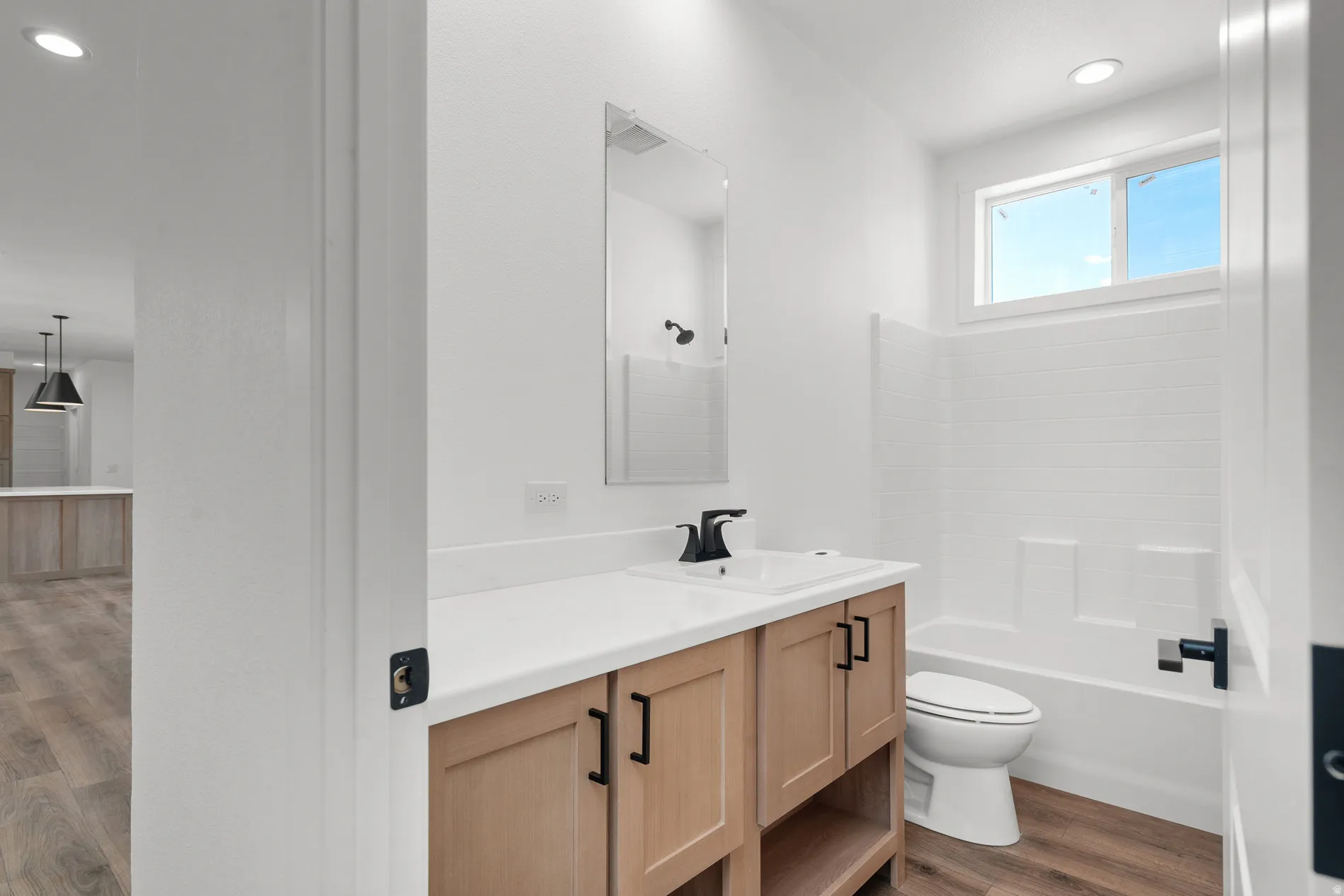 Bathroom featuring a light wood-finish vanity with black hardware, white countertop, and integrated sink