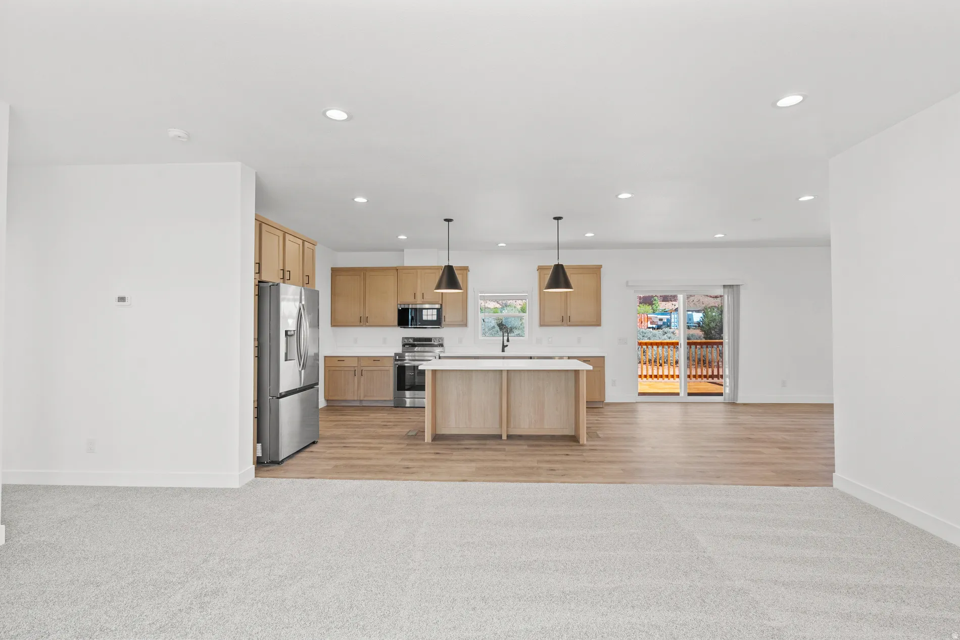 Open-concept kitchen featuring wood-finish cabinetry, stainless steel appliances, a center island with pendant lighting, and wood-finish flooring extending to a glass sliding door
