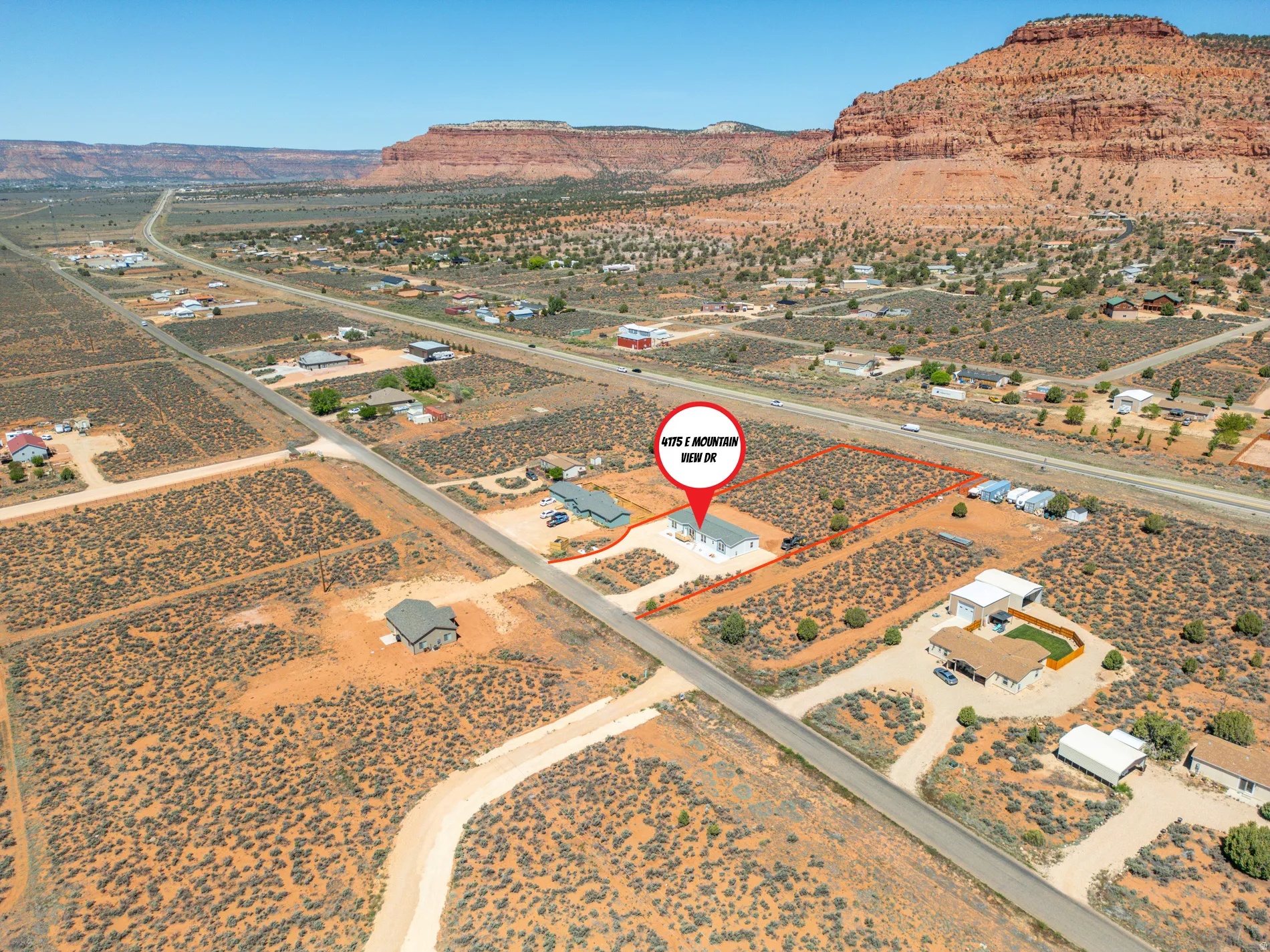 Expansive desert landscape with a single-story residence and detached garage, bordered by a paved road