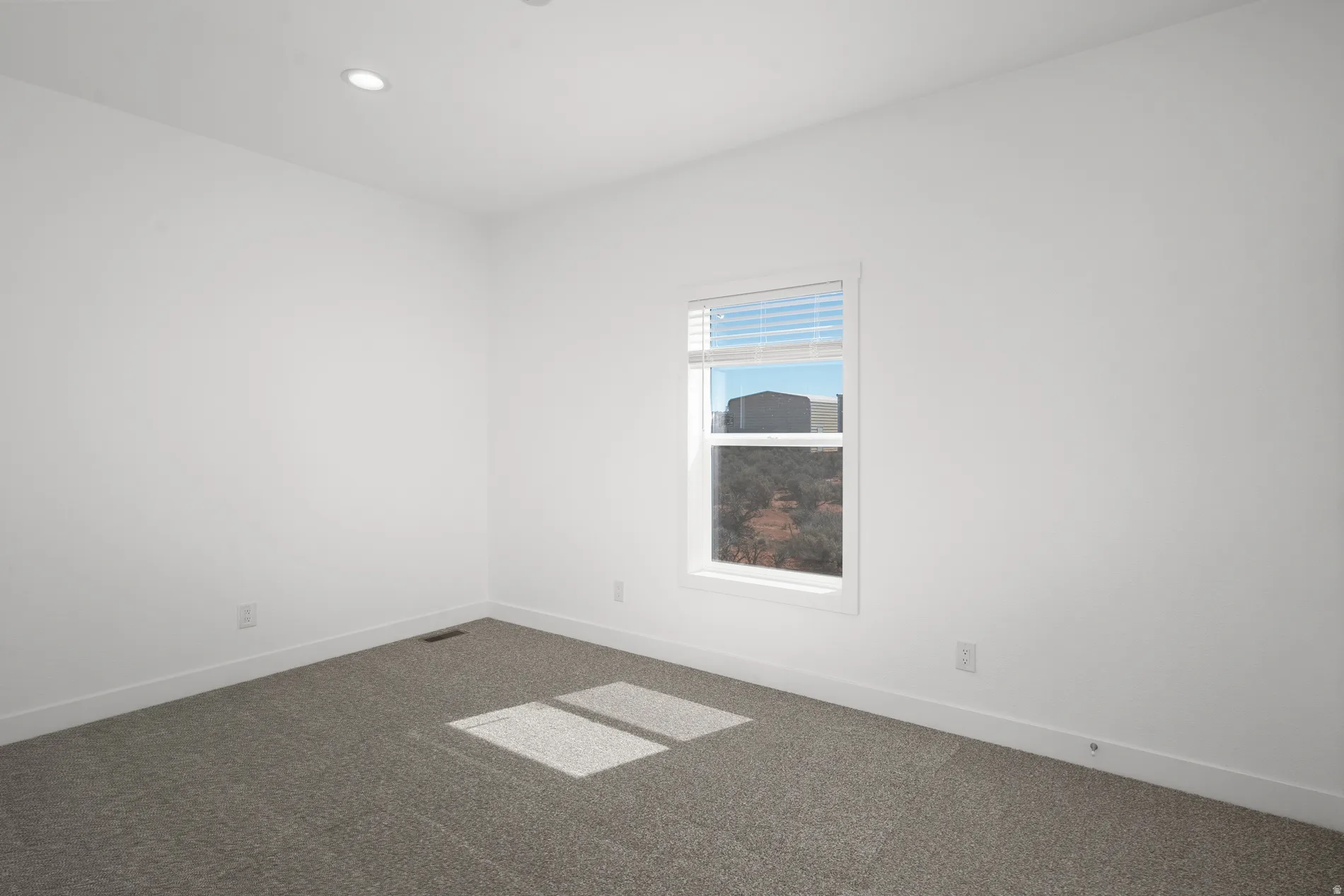 Carpeted room with a single window featuring white blinds, recessed ceiling lighting, and crisp white walls